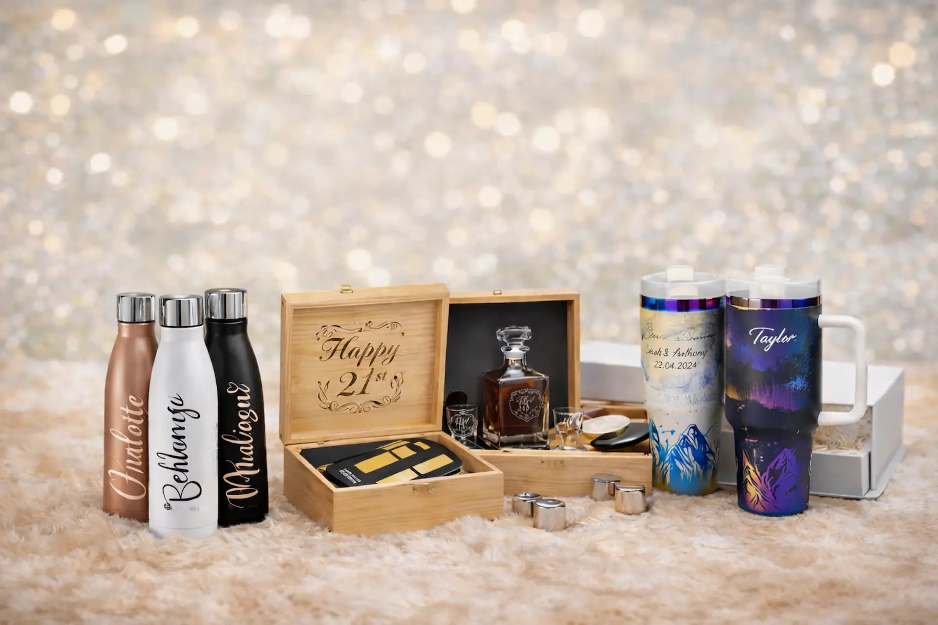 Personalized tumblers and a wooden box with a bottle of whiskey on a textured surface with a blurred background.